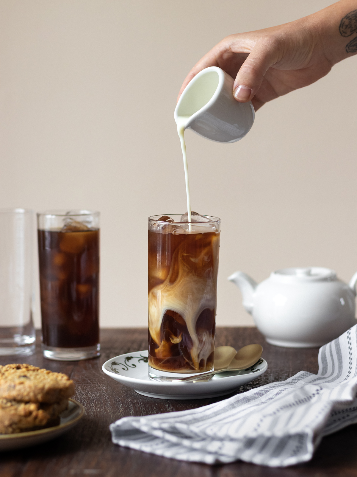 Crop person pouring cream into iced coffee for breakfast